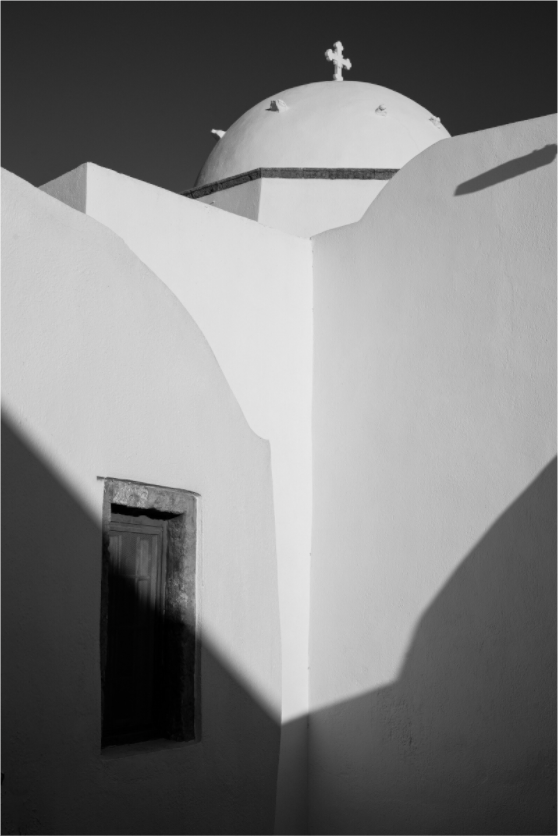 A black and white fine art photograph of a traditional church in Emborio, Santorini. Strong sunlight and geometric shadows reveal the sculptural forms of Cycladic architecture.