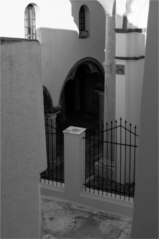 Black and white fine art photograph of a shadowed arched entrance and traditional architecture in Emborio, Santorini.