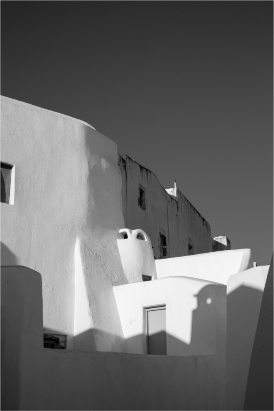 Black and white fine art photograph of sunlit Cycladic architecture and deep shadows in Emborio, Santorini.