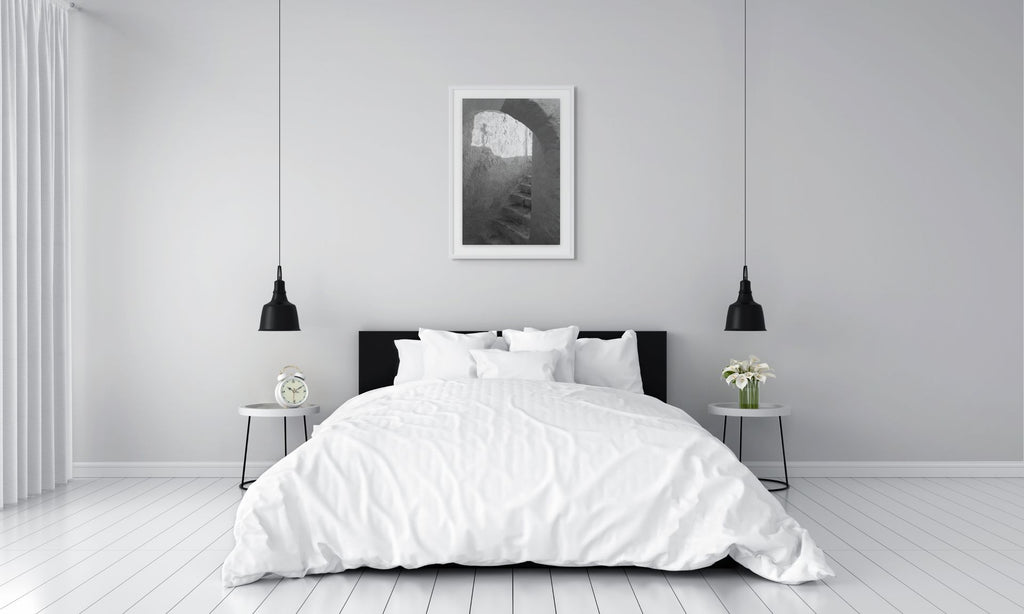The Passage black and white photography print displayed above a modern bed in a minimalist bedroom. White frame and passe-partout