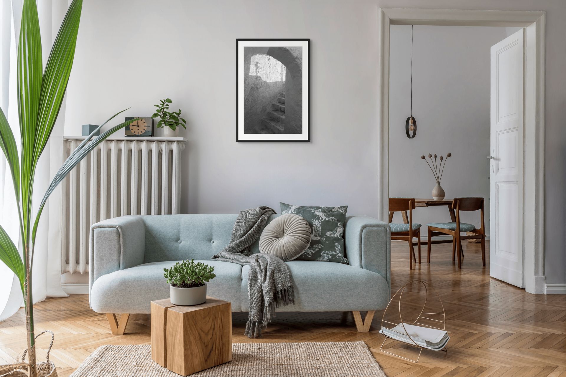 The Passage black and white Santorini fine art print displayed in a Scandinavian-style living room with a light blue sofa and natural wood accents. Black frame and passe-partout.